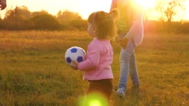 mutlu çocuk çim üzerinde topu ile çalışır, futbol topu atar. Gün batımında bir parkta çocuk topu küçük çocuk ile oynayan aile. anne top küçük kızı ile oynar. Yavaş çekim