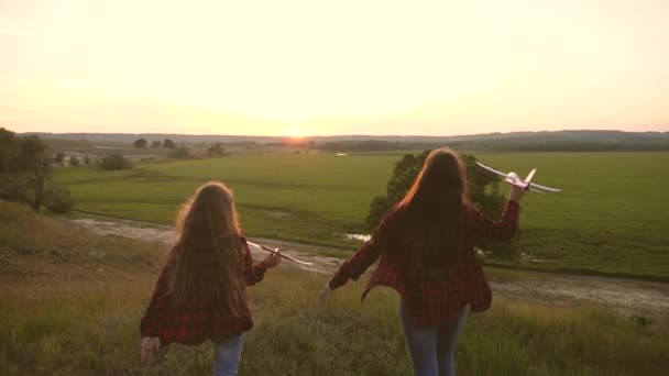 Sogni di volare. Concetto infanzia felice. Due ragazze giocano con un aereo giocattolo al tramonto. Bambini sullo sfondo del sole con un aereo in mano. Silhouette di bambini che giocano sull'aereo — Video Stock