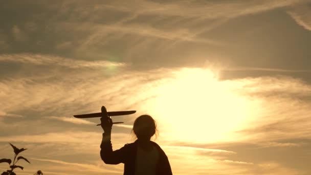 Criança corre ao sol com um avião na mão. Silhueta de crianças brincando no avião. Menina brincando com um avião de brinquedo ao pôr do sol. Sonhos de voar. O conceito de uma infância feliz . — Vídeo de Stock