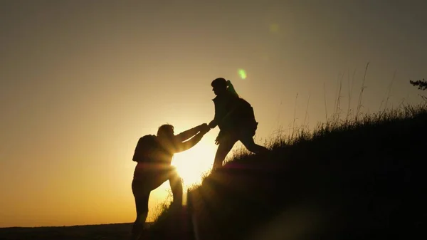 Γυναίκα ταξιδιώτη απλώνει ένα χέρι σε έναν άνδρα αναρρίχηση στην κορυφή ενός λόφου. Οι ταξιδιώτες σκαρφαλώνουν στο γκρεμό κρατώντας τα χέρια. ομαδική δουλειά επιχειρηματιών. Ευτυχισμένη οικογένεια σε διακοπές. τουρίστες αγκαλιά στην κορυφή του βουνού — Φωτογραφία Αρχείου