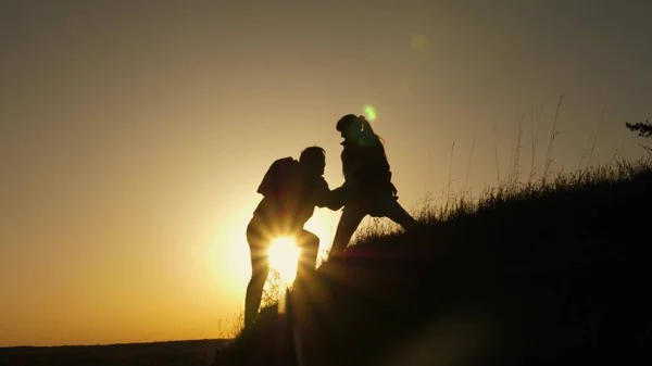 Woman traveler stretches a hand to a man climbing to the top of a hill. travelers climb the cliff holding hands. teamwork of business people. Happy family on vacation. tourists hug on top of mountain — Stock Photo, Image