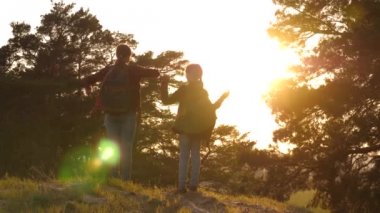 Iki kız seyahat, ormanda yürümek ve tepede ellerini sallamak. Yürüyüşçü Kız. kızlar bir kır yolda sırt çantaları ile seyahat. Tatil seyahatlerinde mutlu bir aile. spor turizmi konsepti.