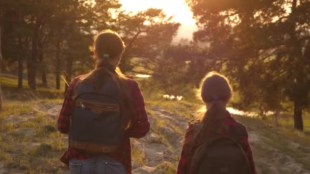 Wandelaar meisje. twee meisjes reizen, lopen door bos en zwaaien hun handen op heuvel. meisjes reizen met rugzakken op een landweg. Gelukkige familie op vakantie reizen. sport toerisme concept. — Stockvideo