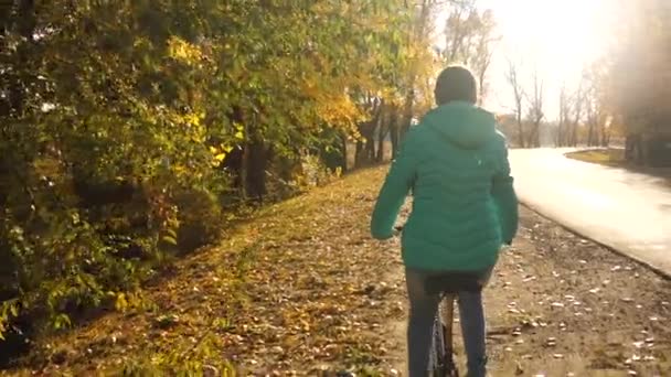 Jong meisje rijdt fiets aan de kant van de weg in de herfst Park op een achtergrond van gele bomen. sportieve fietstocht. — Stockvideo