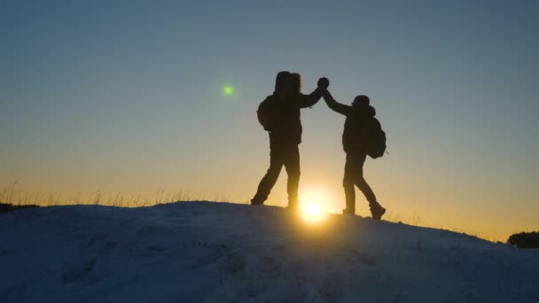 Climbers meet on top of snowy mountain and enjoy their success, raise their hands and jump joyfully. teamwork businessman. Men tourists with backpacks reached top of hill in winter a sunset. — Stock Video