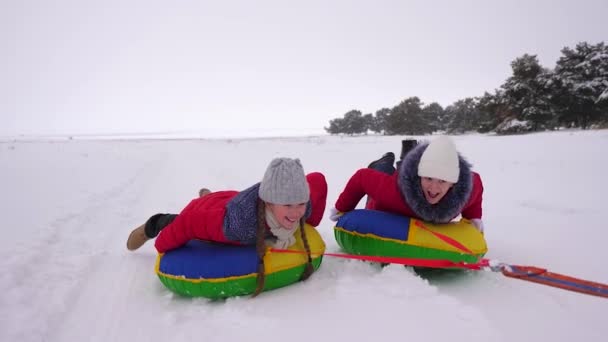 Niños en chaquetas rojas en invierno paseo a través de la nieve en un tubo de nieve inflable y en trineo. deporte niñas relajarse en el parque de invierno para las vacaciones de Navidad. Movimiento lento — Vídeos de Stock