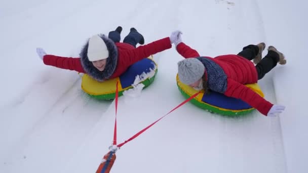 Roliga barn i röda jackor på vintern rida genom snön på slädar och en uppblåsbar snö pipe och spela superhjältar. Glada tjejer avkopplande i Vinterparken för julhelgen. Slow motion — Stockvideo