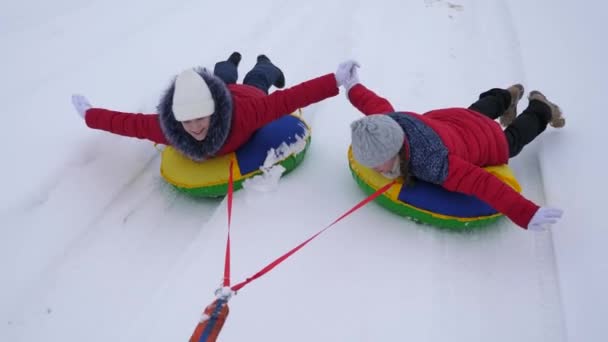 vicces gyerekek télen piros zakó hóban szánkót és egy felfújható hó cső lovagolni, és játszani szuperhősök. Boldog lány pihentető téli park, a karácsonyi ünnepek. Lassú mozgás