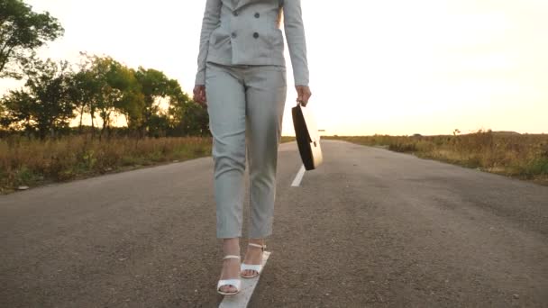 Mujer de negocios con piernas largas caminando por el camino. mujer de negocios camina por la carretera con un maletín negro en la mano, de cerca — Vídeos de Stock