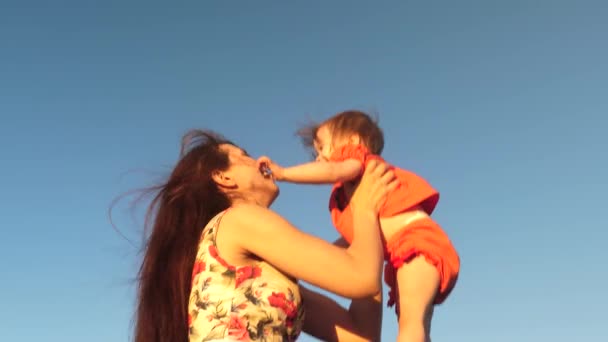 ママは青い空に対して小さな子供と遊びます。母は娘を空に投げ捨てる。空に対して夜に遊ぶ幸せな家族。母親は赤ちゃんを投げ出し、赤ちゃんは笑顔です。スローモーション撮影. — ストック動画