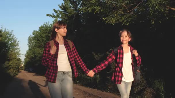 Hiker Girl. adolescentes viajan y se toman de la mano. niños viajeros. chicas con mochilas están en el camino del campo en el sol. concepto de turismo deportivo y viajes . — Vídeos de Stock