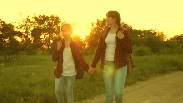 Hiker Girl. teen girls travel and hold hands. children travelers. girls with backpacks are on the country road in the sun. concept of sports tourism and travel. — Stock Video