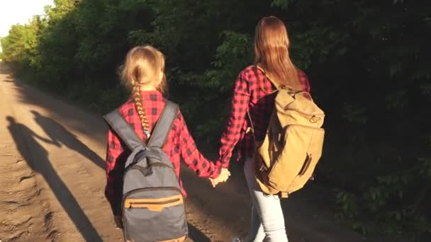 Dziewczyna Hiker. dziewczyny z plecaki są na drodze wiejskiej w słońcu. koncepcja turystyki sportowej i podróży. dzieci. nastolatków dziewcząt podróżować i trzymać ręce. — Wideo stockowe