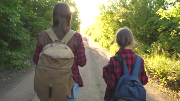 Mamma e figlia viaggiano con uno zaino contro il cielo. turisti madre e bambino vanno al tramonto in montagna. famiglia felice in vacanza viaggia. concetto di turismo sportivo . — Video Stock