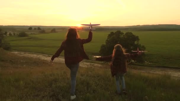 Dromen van vliegen. Gelukkige kindertijd concept. Twee meisjes spelen met een speelgoedvliegtuig bij zonsondergang. Kinderen op de achtergrond van de zon met een vliegtuig in de hand. Silhouet van spelende kinderen in het vliegtuig — Stockvideo