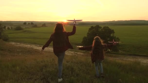 Sueños de volar. Concepto de infancia feliz. Dos chicas juegan con un avión de juguete al atardecer. Niños en el fondo del sol con un avión en la mano. Silueta de niños jugando en el avión — Vídeo de stock