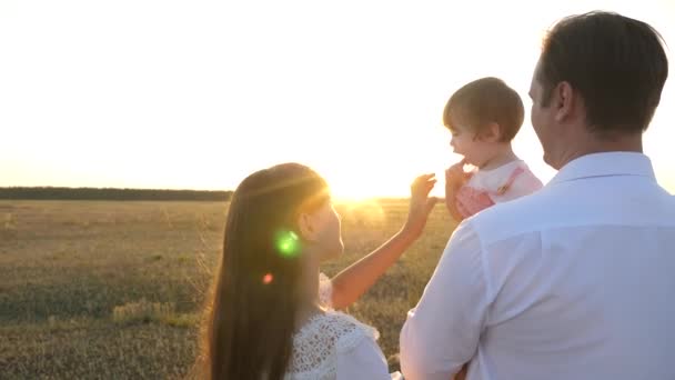 A família brinca com o bebê ao pôr-do-sol. O pai e a mãe andam com a filha nos braços ao pôr-do-sol. pai com filhas descansando no parque. conceito de família feliz e infância . — Vídeo de Stock