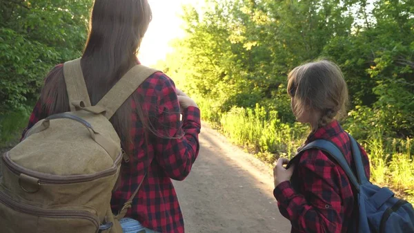 Máma s dcerou cestují s batohu proti nebi. Turisté a matka a dítě jdou do hor na západ slunce. šťastná rodina na dovolené. koncepce sportovního turismu. — Stock fotografie