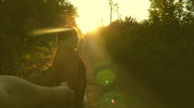 Sırt çantası ile Hiker kız elle adam tutar ve onu yol açar. Genç çift el gün batımı ışınları ülke yolda seyahat tutarak. turistler bir takımda çalışmak. Eller aşk seyahat vardır. Benimle gel