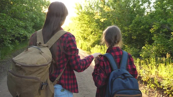 Mamma e figlia viaggiano con uno zaino contro il cielo. turisti madre e bambino vanno al tramonto in montagna. famiglia felice in vacanza viaggia. concetto di turismo sportivo . — Foto Stock