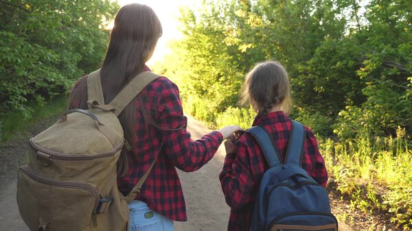 Mom and daughter travel with a backpack against the sky. tourists mother and child go to sunset in the mountains. happy family on vacation travels. sports tourism concept.