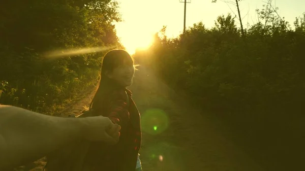 Hiker flicka med ryggsäck håller mannen för hand och leder honom. Ungt par håller händer reser på landsväg i strålar av solnedgång. arbeta i ett team av turister. händer i kärlek reser. Kom med mig — Stockfoto