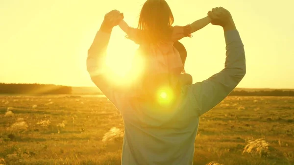 Папа танцует на плечах с дочерью на солнце. Отец путешествует с ребенком на плечах в лучах заката. Ребенок с родителями гуляет на закате. счастливая семья отдыхает в парке. семейная концепция — стоковое фото