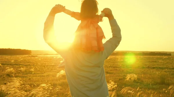 Papa dansant sur ses épaules avec sa fille au soleil. Père voyage avec bébé sur ses épaules dans les rayons du coucher du soleil. Un enfant avec ses parents marche au coucher du soleil. famille heureuse reposant dans le parc. concept de famille — Photo