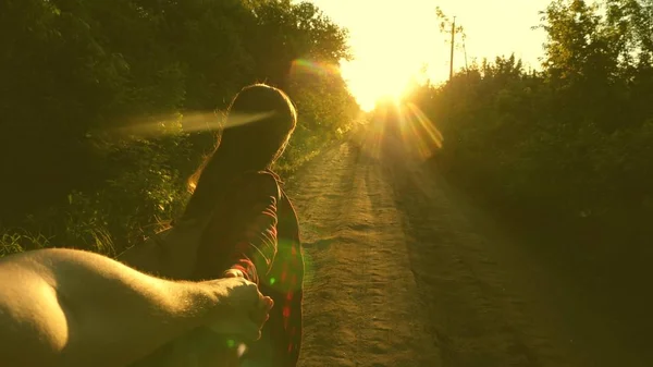Hiker Girl with backpack holds man by hand and leads him. Young couple holding hands traveling on country road in rays of sunset. work in a team of tourists. hands in love are traveling. come with me — Stock Photo, Image