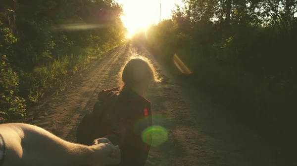 Wandermädchen mit Rucksack hält Mann an der Hand und führt ihn. junges Paar Händchen haltend auf einer Landstraße im Sonnenuntergang. Arbeit in einem Team von Touristen. Verliebte Hände sind unterwegs. Komm mit mir — Stockfoto