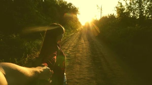 Hiker Girl with backpack holds man by hand and leads him. Young couple holding hands traveling on country road in rays of sunset. work in a team of tourists. hands in love are traveling. come with me — Stock Photo, Image