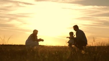 Annem ve babam gün batımında parkta kızlarıyla oynuyor. Çocuk ilk adımları alır. Mutlu aile güneş ışınları çocuk ile oynuyor. Bebek babasından anneme gider ve gülüyor. Yavaş hareket.