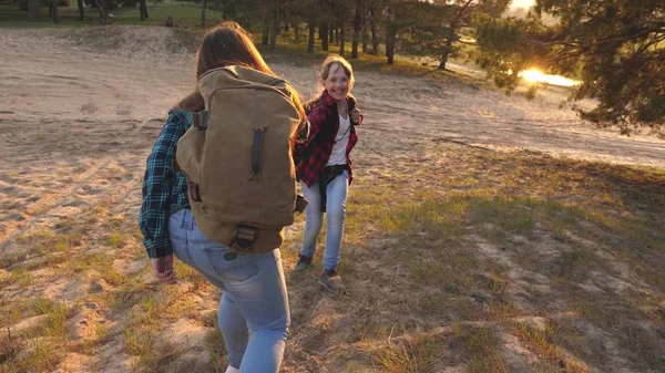 happy girls travel in forest, climb hill, give a helping hand. Hiker Girl. family walks in woods. girls travel with backpacks on country road. Happy family on vacation travels. sports tourism concept.