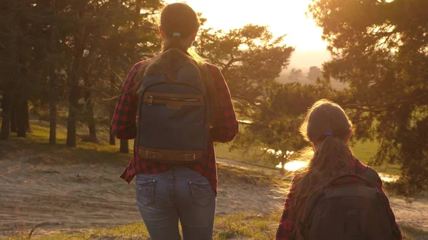 Ragazza escursionista. due ragazze viaggiano, camminano attraverso la foresta e agitano le mani sulla collina. le ragazze viaggiano con gli zaini su una strada di campagna. Famiglia felice in vacanza. concetto di turismo sportivo . — Foto Stock