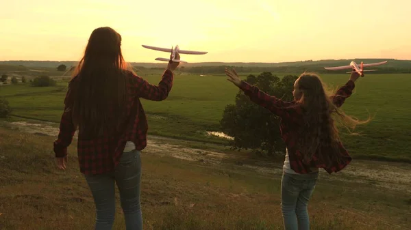 Sogni di volare. Concetto infanzia felice. Due ragazze giocano con un aereo giocattolo al tramonto. Bambini sullo sfondo del sole con un aereo in mano. Silhouette di bambini che giocano sull'aereo — Foto Stock