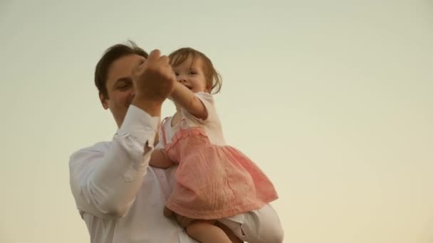 Papá bailando sobre sus hombros con su hija al sol. Padre viaja con el bebé sobre sus hombros en rayos de atardecer. Un niño con padres camina al atardecer. familia feliz descansando en el parque. concepto familiar — Vídeo de stock