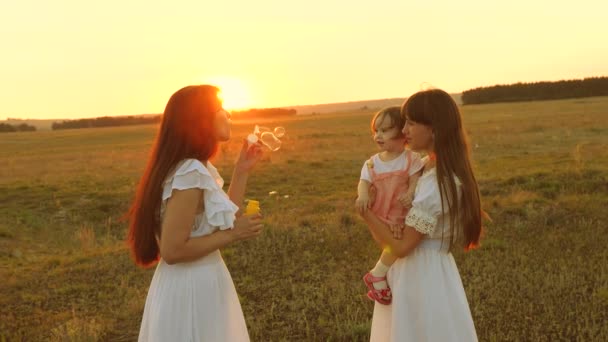 Dochters verheugen en glimlach, bubbels vliegen in Park bij zonsondergang. Slow Motion. Gelukkige moeder spelen met kinderen blazen zeepbellen. concept van een gelukkige familie. kind, zus en moeder spelen bij Sunrise. — Stockvideo