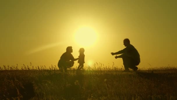 Happy child goes from mother to father. parents play with their little daughter. mother and Dad play with their daughter in sun. young family in the field with a child 1 year. family happiness concept — Stock Video