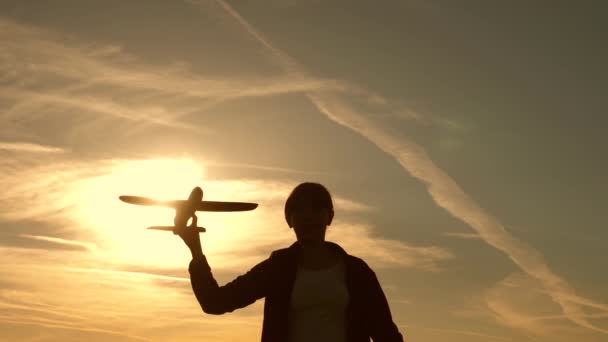 Bambini sullo sfondo del sole con un aereo in mano. ragazza giocare con un aereo giocattolo al tramonto. Sogni di volare. Concetto infanzia felice. Silhouette di bambini che giocano sull'aereo — Video Stock