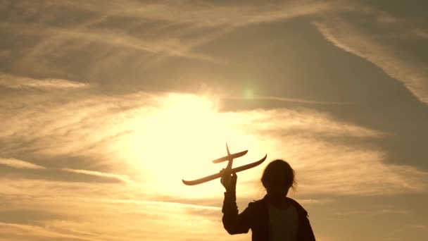 Álmok-ból repülés. Gyermekek a háttérben a nap egy repülőgép a kezében. Sziluettje gyerekek játszanak a gépen. lány játszani egy játék sík naplementekor. Boldog gyermekkori koncepció. — Stock videók