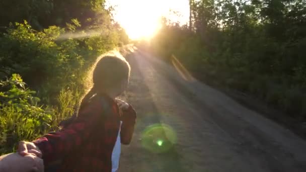 Mani innamorate sono in viaggio. Vieni con me. Hiker Girl con lo zaino tiene l'uomo per mano e lo conduce. Giovane coppia che si tiene per mano viaggiando su strada di campagna in raggi di tramonto. lavorare in un team di turisti — Video Stock