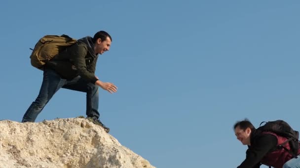 Teamwork of business people. tourists give hand to each other, climbing to top of the hill. team of male travelers goes to victory and success. two climbers climb one after another on white rock. — Stock Video