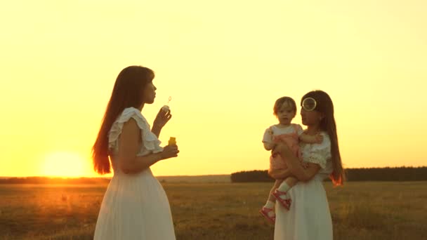 Lycklig mamma leker med barn blåser tvål bubblor. Döttrar och mor blåser bubblor i parken vid solnedgången. Slow motion. lyckligt familjekoncept. Baby, Syster och mamma spelar i solen. — Stockvideo