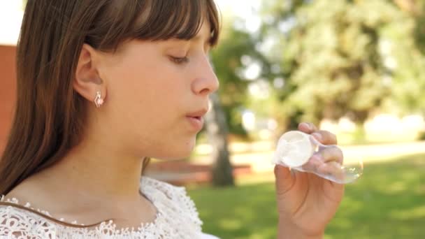 Šťastná dívka foukání krásné mýdlové bubliny v parku na jaře, v létě a s úsměvem. Zpomalený pohyb. mladá dívka projíždějící městem v parku. — Stock video