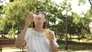 Güzel kız ilkbaharda parkta sabun kabarcıkları üfleme, yaz ve gülümseyerek. Yavaş çekim. parkta oynayan ve kamera merceği içine kabarcıklar üfleme genç kız.