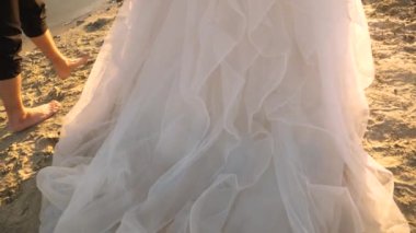 damat yalınayak ve beyaz bir elbise gelin nehir boyunca sahil boyunca yürümek. aşık çift su yakınında yaz aylarında kum üzerinde yürür. Close. Yavaş çekim. mutlu aile kavramı.