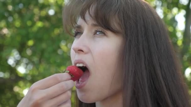 Bella ragazza mangiare aspro fragola ruga e sorridente. primo piano. Vitamina e bacca dieta per le donne. ragazza felice mangiare fragole in estate in giardino. Delizioso dessert alla fragola . — Video Stock