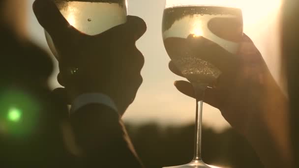 Champagner funkelt und schäumt in der Sonne. Verliebte Paare halten Weingläser mit Sekt vor dem Hintergrund des Sonnenuntergangs. Nahaufnahme. Teamwork eines liebenden Paares. Erfolg und Sieg feiern. Zeitlupe — Stockvideo