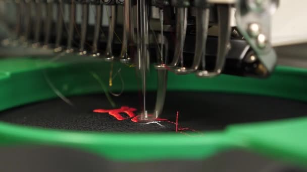 自動ミシン。ロボットミシン。黒い布に赤い糸が付いた自動機械刺繍パターン。ロボティクスは、生産ラインを調整する上で動作します. — ストック動画