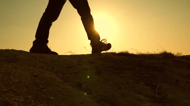 Een moedige man-reiziger, klimmen naar de top van een berg, wandelen langs een pad langs een gevaarlijke rotsachtige heuvelrug. Steile muur die een prachtig uitzicht op de zonsondergang opent. Slow Motion. Close-up. — Stockvideo